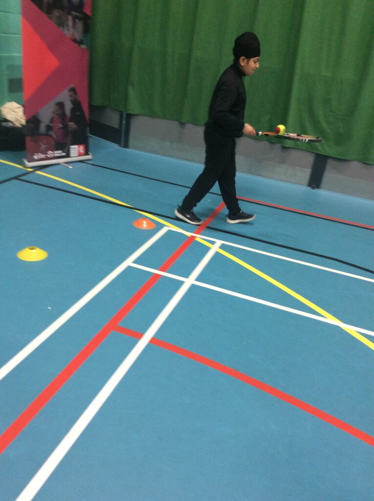 A male student is pictured walking around in the Sports Hall, holding out a Tennis racket and balancing a ball on it.