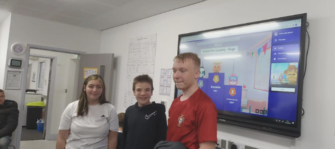 Three students are pictured stood at the front of the classroom, about to speak to their peers.