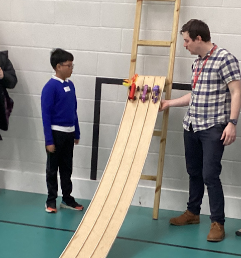A student and a teacher watching the student's project vehicle rolling down a ramp