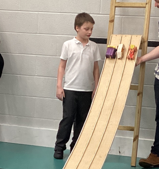 A student and a teacher watching the student's project vehicle rolling down a ramp