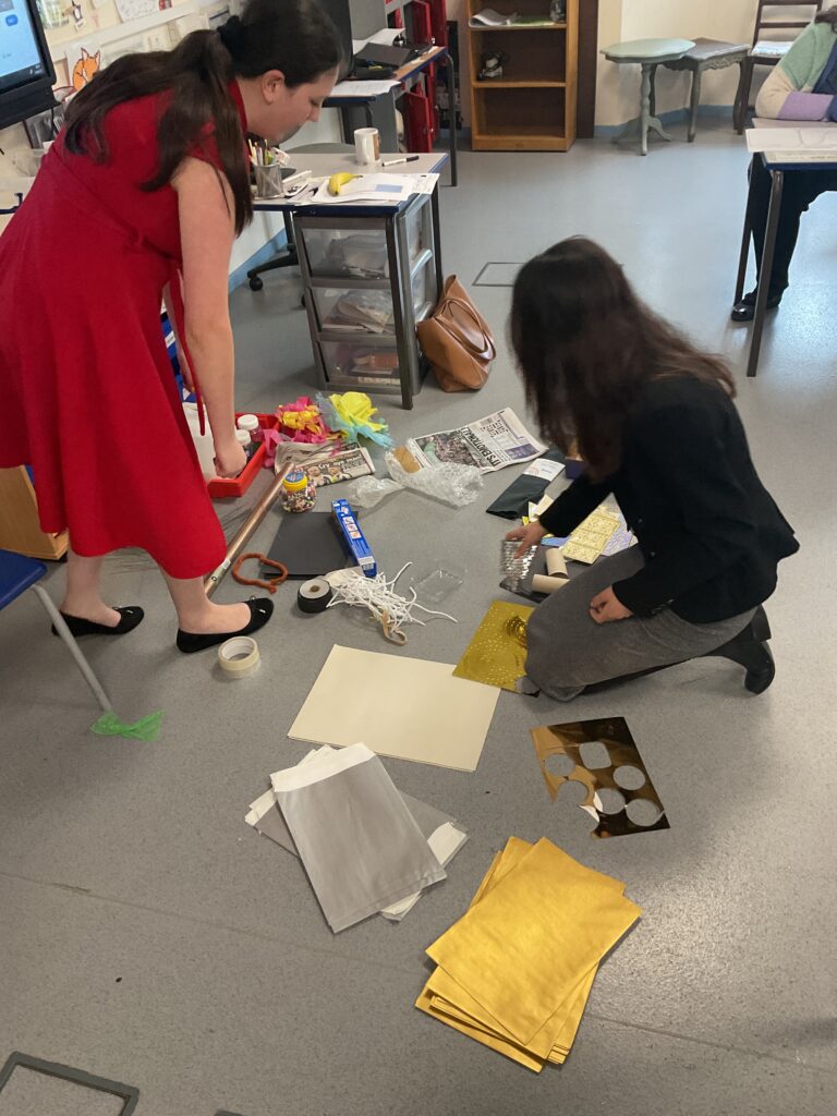 Teachers in a classroom sorting through various arts and crafts materials on the floor