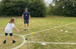 A young pupil taking part in the shot put at Sports day. Watched by a teacher