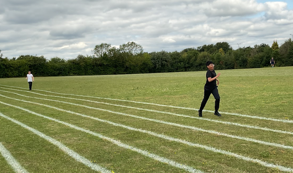 Two pupils running on a grass running track