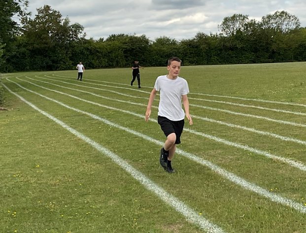 Three pupils taking part in a race on a grass running track