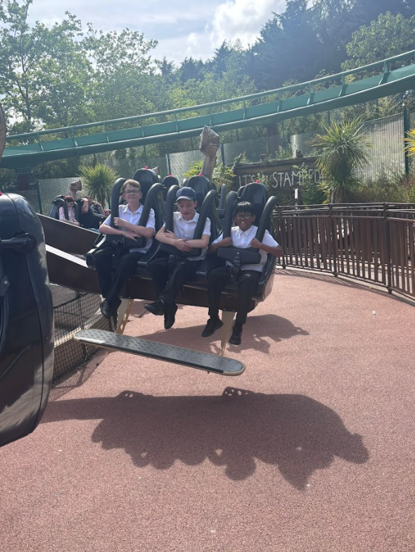 Three boys are strapped into a ride that appears to swing or rotate, with their feet dangling. The ride has a "IT'S THE STAMPEDE" sign in the background, indicating the name of the attraction.