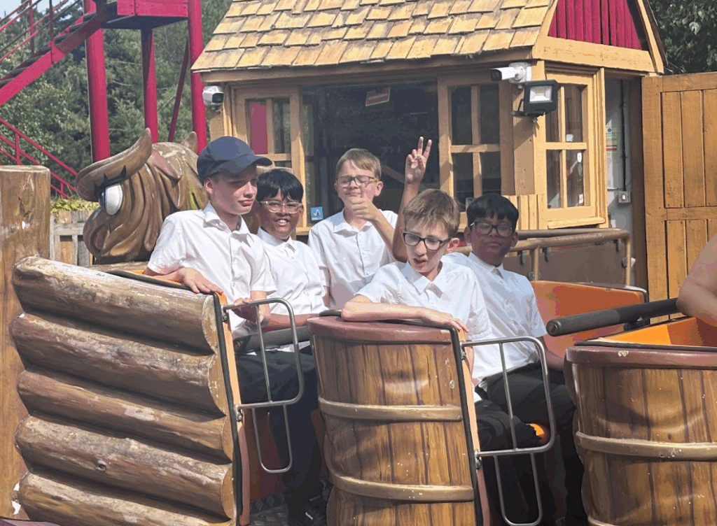 A group of children, again in similar white shirts, are seated in a theme park ride, smiling and appearing to enjoy themselves.