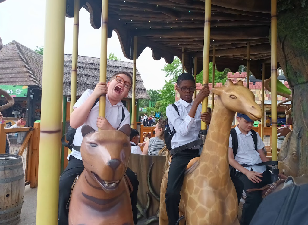Two children are on a carousel-style ride, one on a bear and another on a giraffe, both smiling and appearing to have fun. This is a classic amusement park attraction.