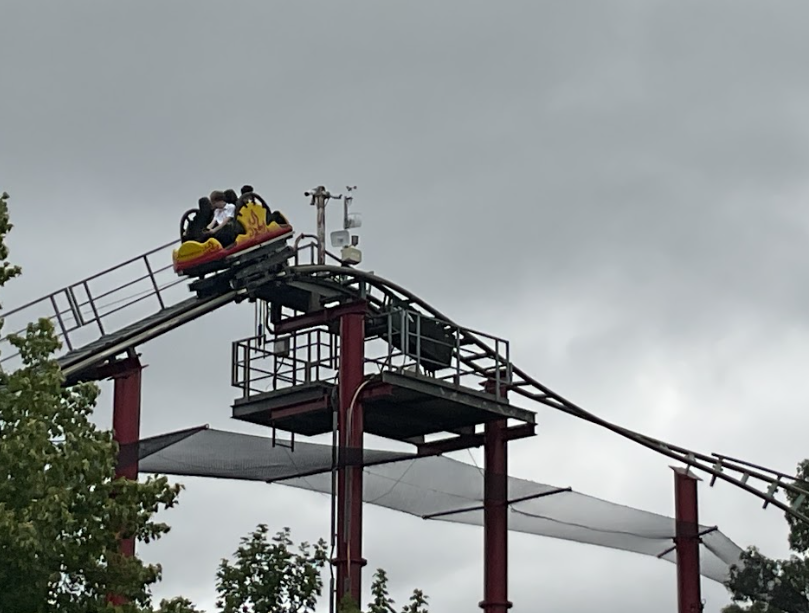 A roller coaster car with people in it is going up a track against a cloudy sky. This indicates the location is also a theme park.