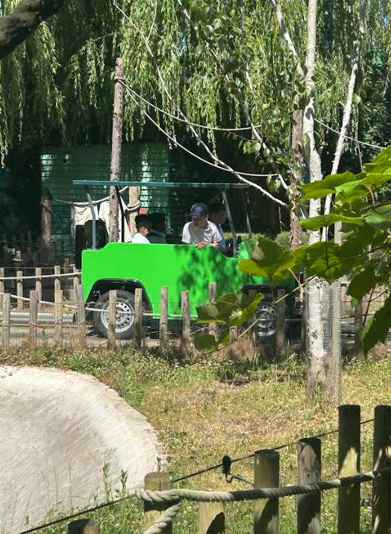 Children are riding in a bright green vehicle that looks like a safari jeep on a track, suggesting a themed ride, possibly through a simulated jungle or animal area.