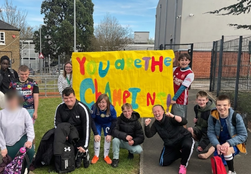 A group of children posing for a picture with two holding a large banner with the words 'You are the Champions!' on it